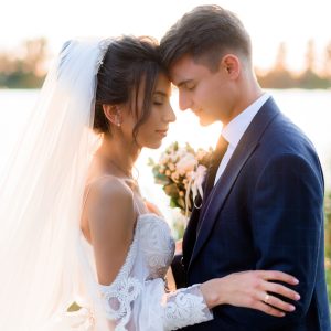 Portrait of beautiful bride and groom with closed eyes are hugging near the water  outdoors in the evening